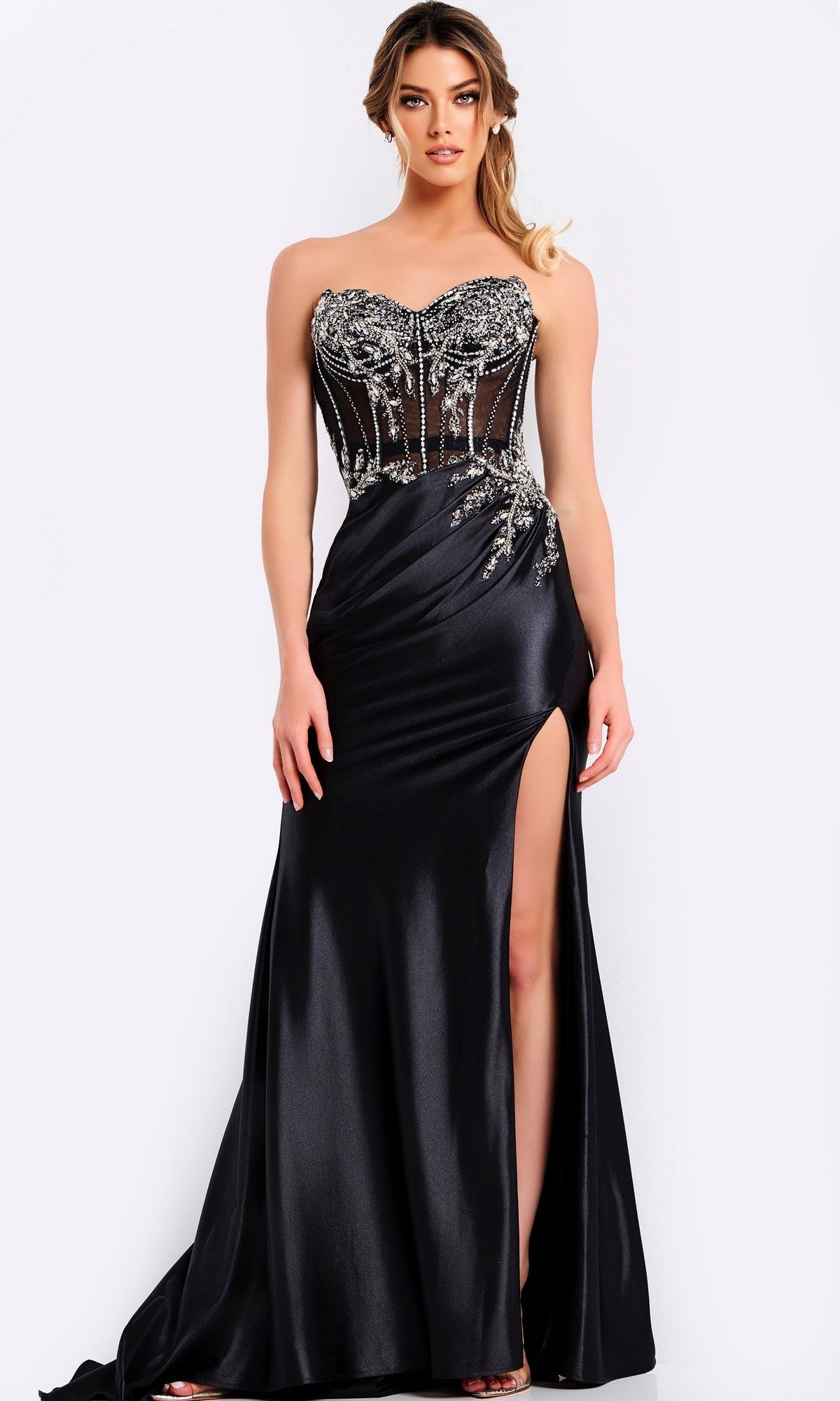 A woman stands against a plain light background wearing the Jovani 49720 long prom dress, featuring a black strapless design with a sheer crystal beaded bodice, satin skirt, side embellishments, and a high thigh slit.